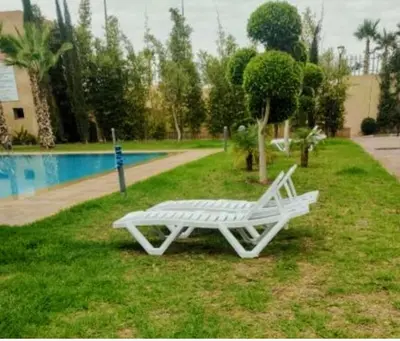 a white bench sitting in the grass near a pool at Un élégant appartement à louer à Marrakech avec deux piscines et une situation en centre ville in Marrakech