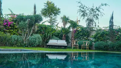 a pool with two chairs and a bench next to a garden at VILLA Atlas in Sraghna