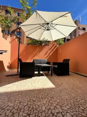 a patio with a table and an umbrella and chairs at Cosy Appartement Famille in Marrakech