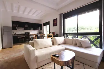 a living room with a white couch and a kitchen at Somptueux appartement avec terrasse et piscines in Marrakech