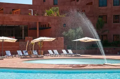 a fountain in a pool with chairs and umbrellas at Palacio Hôtel Condominium Marrakech in Marrakech