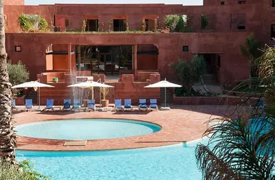 a swimming pool with chairs and umbrellas in front of a building at Palacio Hôtel Condominium Marrakech in Marrakech