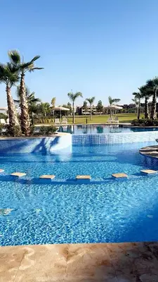 a large swimming pool with blue water and palm trees at Luxueux Prestigia golf city Marrakech in Marrakech