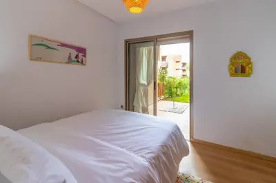 a white bedroom with a bed and a sliding glass door at Peaceful apartment with a garden in Marrakech