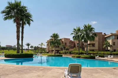 a swimming pool with a chair and palm trees at GOLF PRESTIGIA Résidence TOPAZE in Marrakech