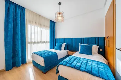 two beds in a room with blue curtains at Luxury and serenity in Prestigia Golf & Pool in Marrakech