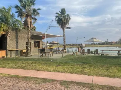a patio with tables and palm trees next to a body of water at appart jardin de l atlas Marrakech Waky Beach Golf Montagne de l Atlas in Marrakech