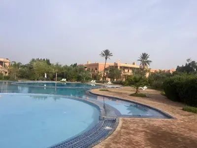 an empty swimming pool in a resort with palm trees at Appartement dans la palmeraie in Marrakech