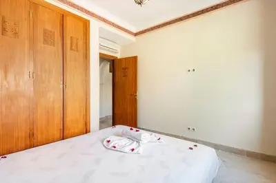 a bedroom with a bed with white sheets and wooden cabinets at Marrakech flat with swimming pool & sunny garden in Marrakech
