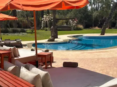 a pool with an umbrella and some chairs and tables at Villa jowehara Palmeraie Marrakech in Marrakech