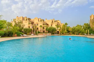 a person in a swimming pool in front of a large building at Appartement de charme residence avec piscine WiFi in Marrakech