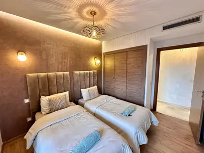 two beds sitting in a room with a window at Pearl Garden Appart 2 chambres Luxe Cosy Moderne in Marrakech