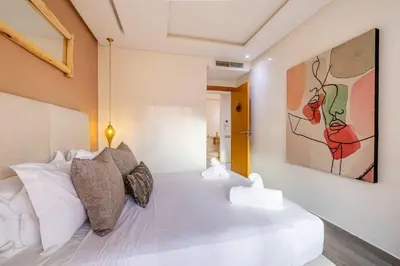 a bedroom with a white bed with a painting on the wall at Grand appartement deux terrasses in Marrakech