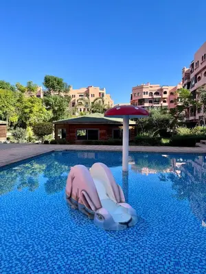 two people in a swimming pool with an umbrella at RENTSUITE APPARTEMENT Premium Village Luxurious Residence in Marrakech