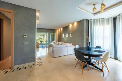 a living room with a table and a white couch at Apart Confort Rez-de-Jardin Piscine Wi-Fi Terrasse in Marrakech