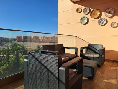a balcony with chairs and a view of a city at Bel appartement à Marrakech dans la résidence Pearl Garden avec piscine située sur la route de Casablanca Sa grande terrasse a une splendide vue sur la ville et les montagnes de l'Atlas A quelques minutes du centre ville et du grand Stade de Marrakech in Marrakech