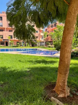 a tree in the grass next to a swimming pool at appartement à coté des palmeraies in Marrakech