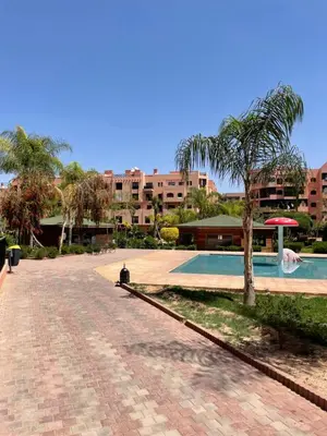 a swimming pool with a palm tree next to a building at appartement à coté des palmeraies in Marrakech
