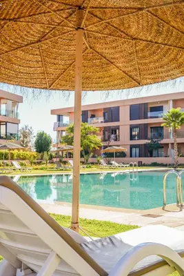 a resort swimming pool with a large umbrella and chairs at Maeva cosy - Clim, Wifi, Jardin à 10min de l'Aéroport in Marrakech
