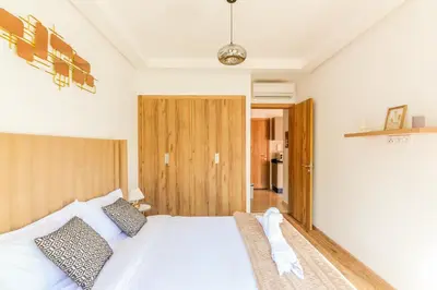 a bedroom with a white bed and a wooden door at Maeva cosy - Clim, Wifi, Jardin à 10min de l'Aéroport in Marrakech