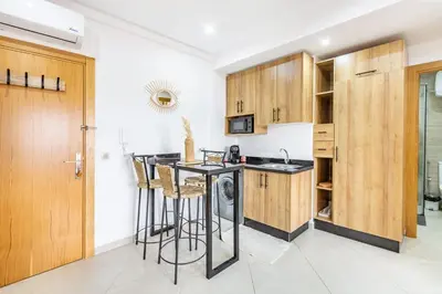 a kitchen with wooden cabinets and a bar with stools at Le COSY CHIC- NEUF - Modern & Chic - Terrasse et Confort - CLIM PARKING et WIFI Gratuit ! GUELIZ in Marrakech