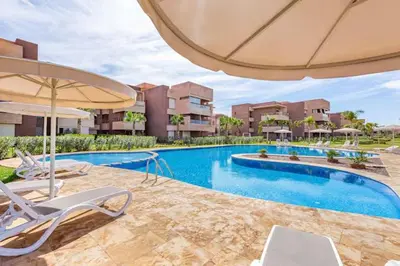 a swimming pool with chairs and an umbrella at Appartement prestigia golf accès piscine in Marrakech