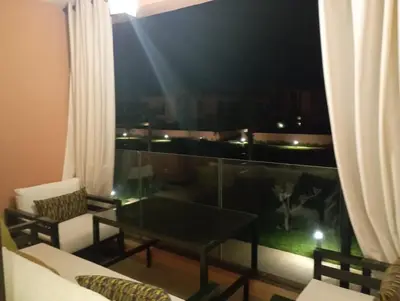 a living room with a table and a balcony at night at Domaine de Noria Isli 2 - Magnifique 2 chambres - Vue directe sur la piscine in Marrakech