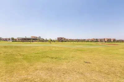 a green field with buildings in the background at Front de piscine en rez de Jardin a Prestigia in Marrakech