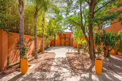 a walkway with trees in front of a building at Villa Simari Palmeraie Marrakech NOUVEAU! Petit déjeuner compris-Entièrement rénovée-Superbe piscine privée chauffée-Personnel de maison inclus-Grand jardin de 2000m2-Terrain de pétanque-Ambiance typique berbère-Havre de paix in Marrakech