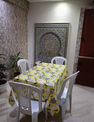 a table with white chairs and a yellow and white table cloth at appartement meuble in Marrakech
