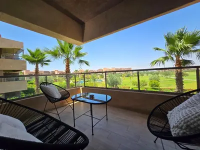 a balcony with chairs and a table and palm trees at Appartement Cosy - vue Piscine - Prestigia JADE in Marrakech