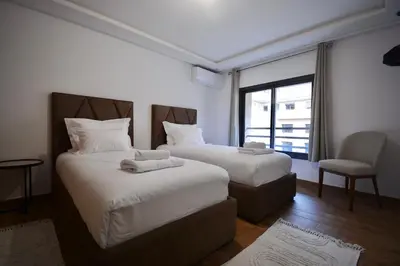 a bedroom with two beds and a chair and a window at Duplex Safiya Suites and Services in Marrakech
