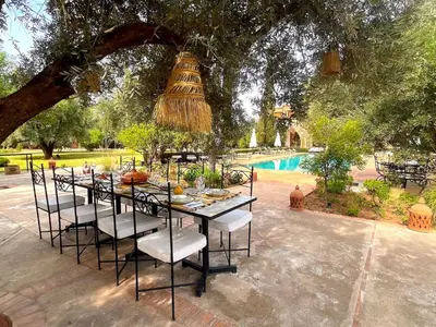 a dining table and chairs under a tree next to a pool at Palais Debora in Marrakech