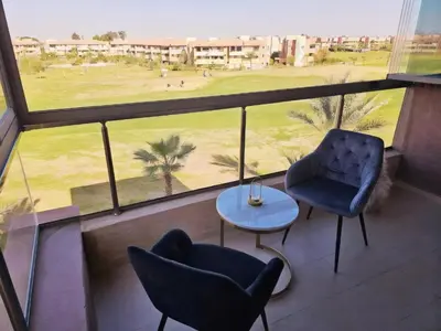 a balcony with two chairs and a table and a golf course at Prestigia Luxury Golf-View Escape in Marrakech