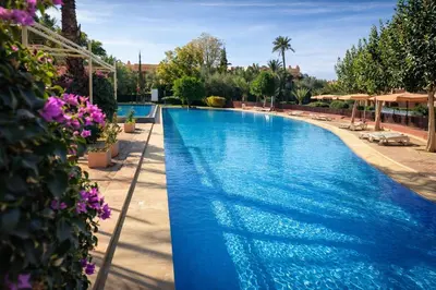 a large swimming pool with blue water and purple flowers at Nohaya - Palmeraie 2 Marrakech Un cadre verdoyant et reposant in Marrakech