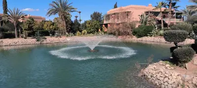a fountain in a pond in front of a building at Nohaya - Palmeraie 2 Marrakech Un cadre verdoyant et reposant in Marrakech