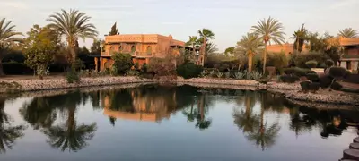 a building with palm trees and a pool of water at Nohaya - Palmeraie 2 Marrakech Un cadre verdoyant et reposant in Marrakech