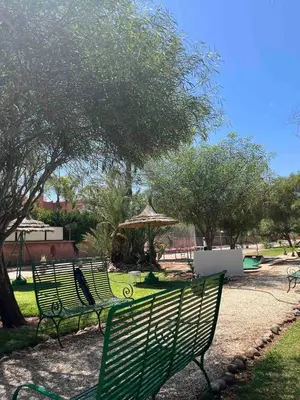 two green benches in a park with an umbrella at Marrakech River Palm in Dar Caïd Layadi