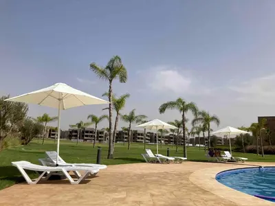 a group of chairs and umbrellas next to a pool at Beautiful residence with pools inMarrakech Golf City in Marrakech