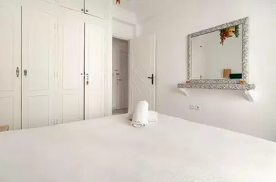 a white bedroom with a white bed and a mirror at Confort et style en pleins centre ville in Marrakech