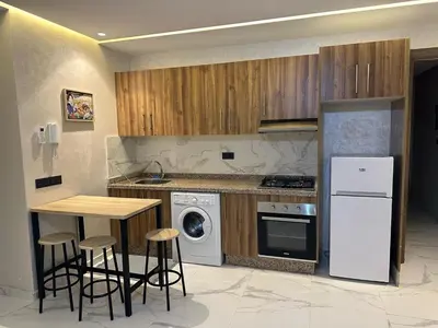 a kitchen with wooden cabinets and a table with stools at Spacieux Appartement avec terrasse coeur de Marrakech in Marrakech