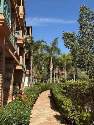 a brick walkway next to a building with palm trees at charmant appartement avec grande piscine & terrasse in Marrakech