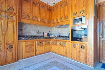 a large kitchen with wooden cabinets and a microwave at Cozy, sunny apartment near the airport in Marrakech