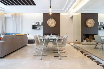 a dining room and living room with a table and chairs at Appartement Cosy avec Parc et Piscine pour femme in Marrakech