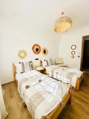 two beds in a room with white walls and wooden floors at Charmant Appartement 2 Room Wifi Marrakech in Marrakech