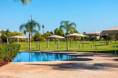 a swimming pool with umbrellas in a park at Elegant Appartement Piscine Golf et Wifi in Marrakech