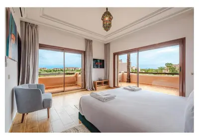 a bedroom with a bed and a chair and windows at Villa Iris Jaccuzi, Piscine 20min Centre in Marrakech
