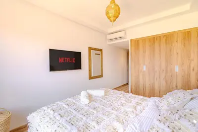a bedroom with a white bed and a tv on the wall at Évasion à NORIA - Vue Piscine et Charme Local in Marrakech