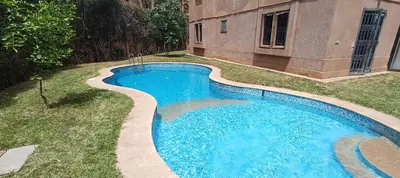 a swimming pool in the grass next to a building at Rez-de-chaussée avec piscine in Marrakech