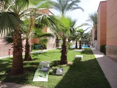 a park with palm trees and a bench and a building at Riad Marrakech - Piscine -Wifi- résidence qarya essyahia in Marrakech